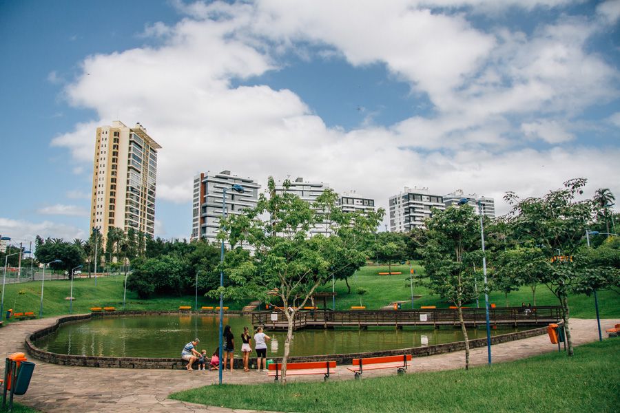 Parque urbano com lago, pessoas, árvores e edifícios ao fundo